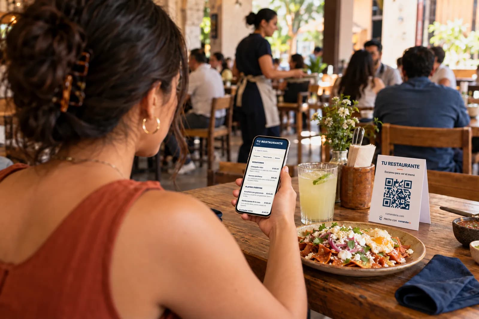 A guest in a restaurant browses the “Tu Restaurante” digital menu on her phone; on the table, the card with the QR code